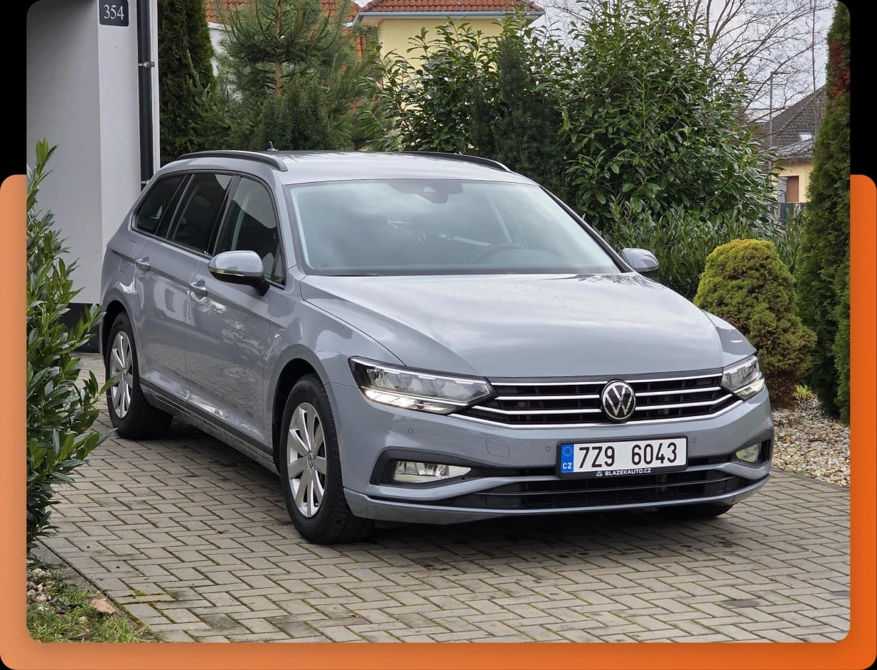 Šedý vůz Volkswagen stojí na dlážděném příjezdu u domu obklopeného zelení