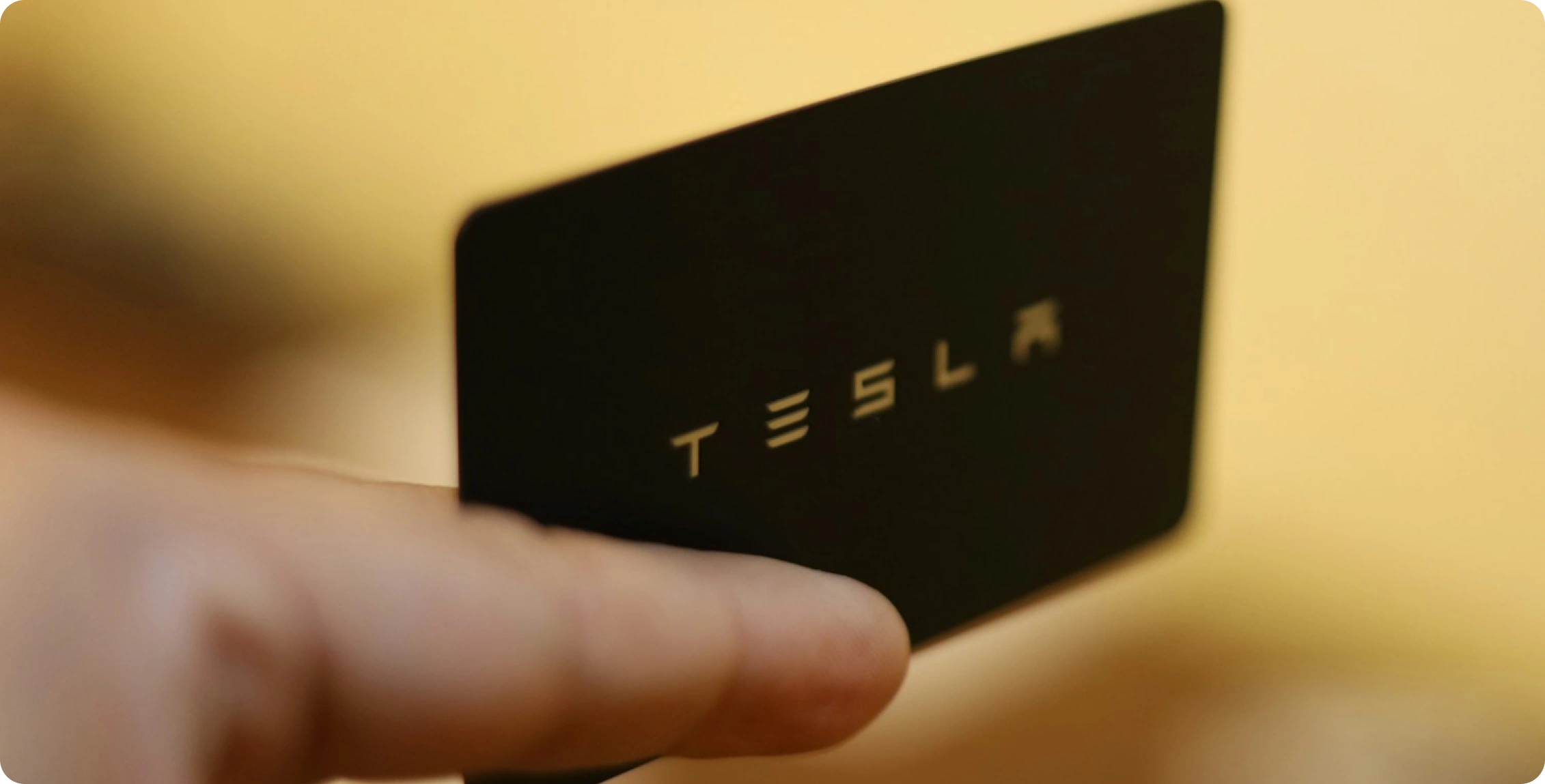 Ruka drží černou kartu s nápisem „TESLA“ v rozostřeném pozadí