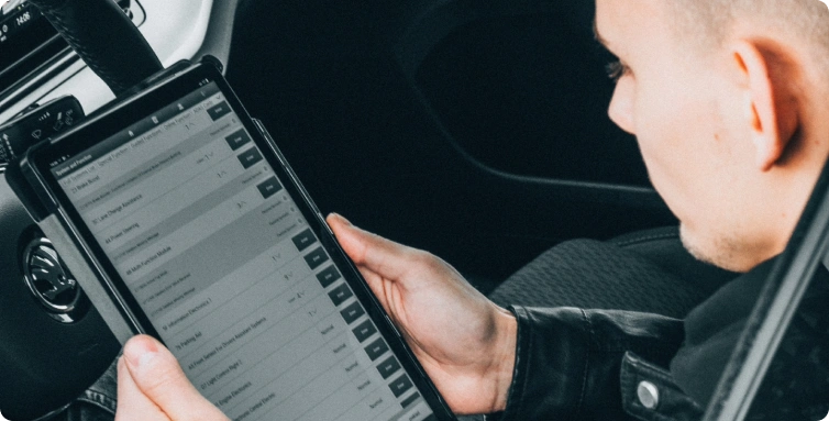Mechanik sedí v autě a drží tablet s diagnostickými údaji