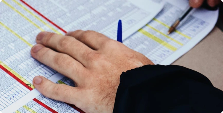 Detail ruky položené na tištěné tabulce s čísly, vedle je propiska připravená k vyplňování