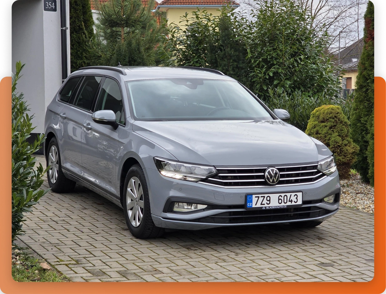 Šedý vůz Volkswagen stojí na dlážděném příjezdu u domu obklopeného zelení